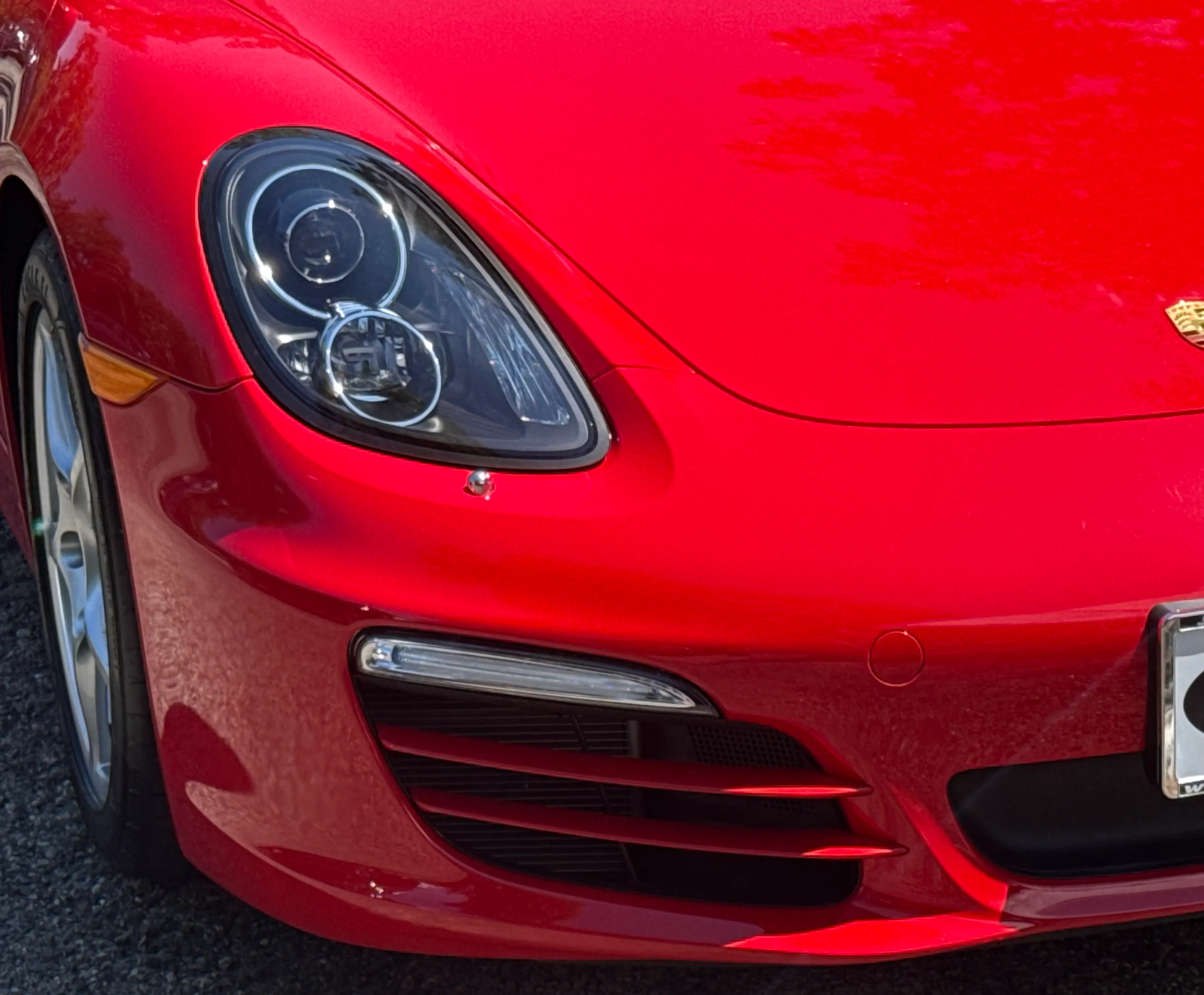 Same Porsche Boxster front bumper corner after repair, gloss red paint smooth and color-matched.