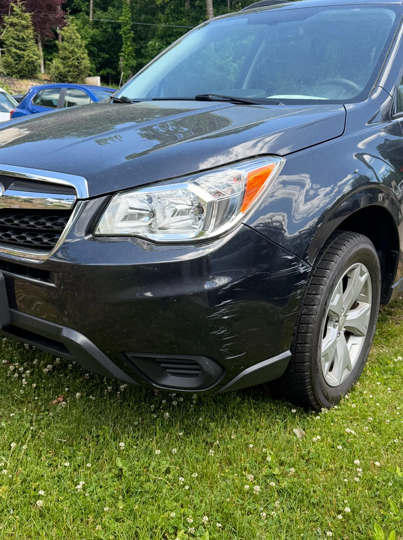Dark gray Subaru Forester front bumper with visible scratches on the driver-side corner above the wheel, before repair.